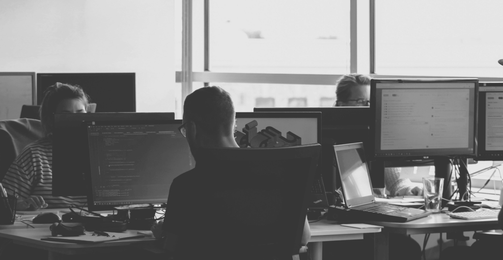 This image of colleagues working at a computer bank illustrates our discussion topic: NIS2, the changes for your organization, and the relevance of Corporate Domain Management.